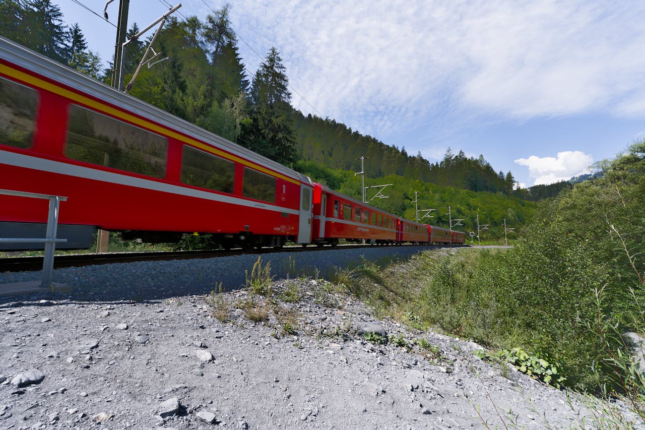 Vibrant red train traveling through lush Swiss mountains on a sunny day, highlighting scenic beauty.